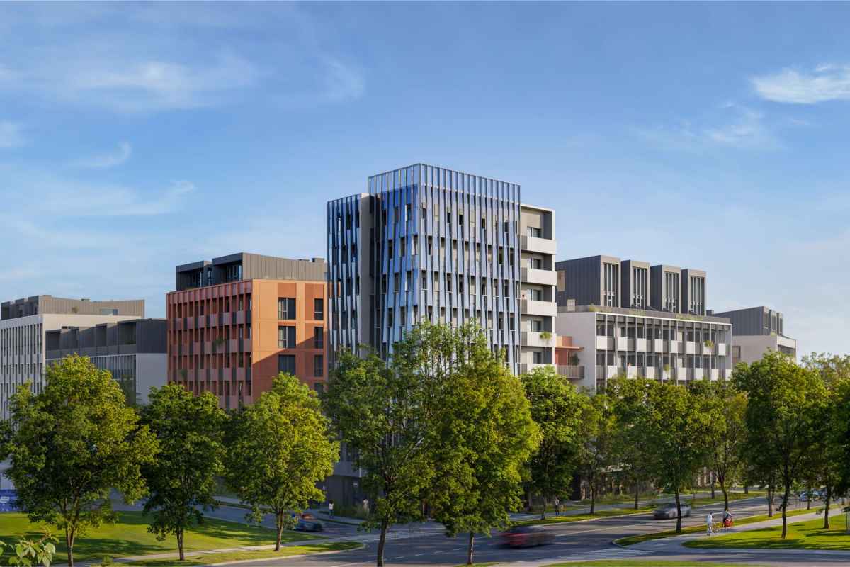 Daugiabučių namų kompleksas su žaliais medžiais prie gatvės saulėtą dieną.